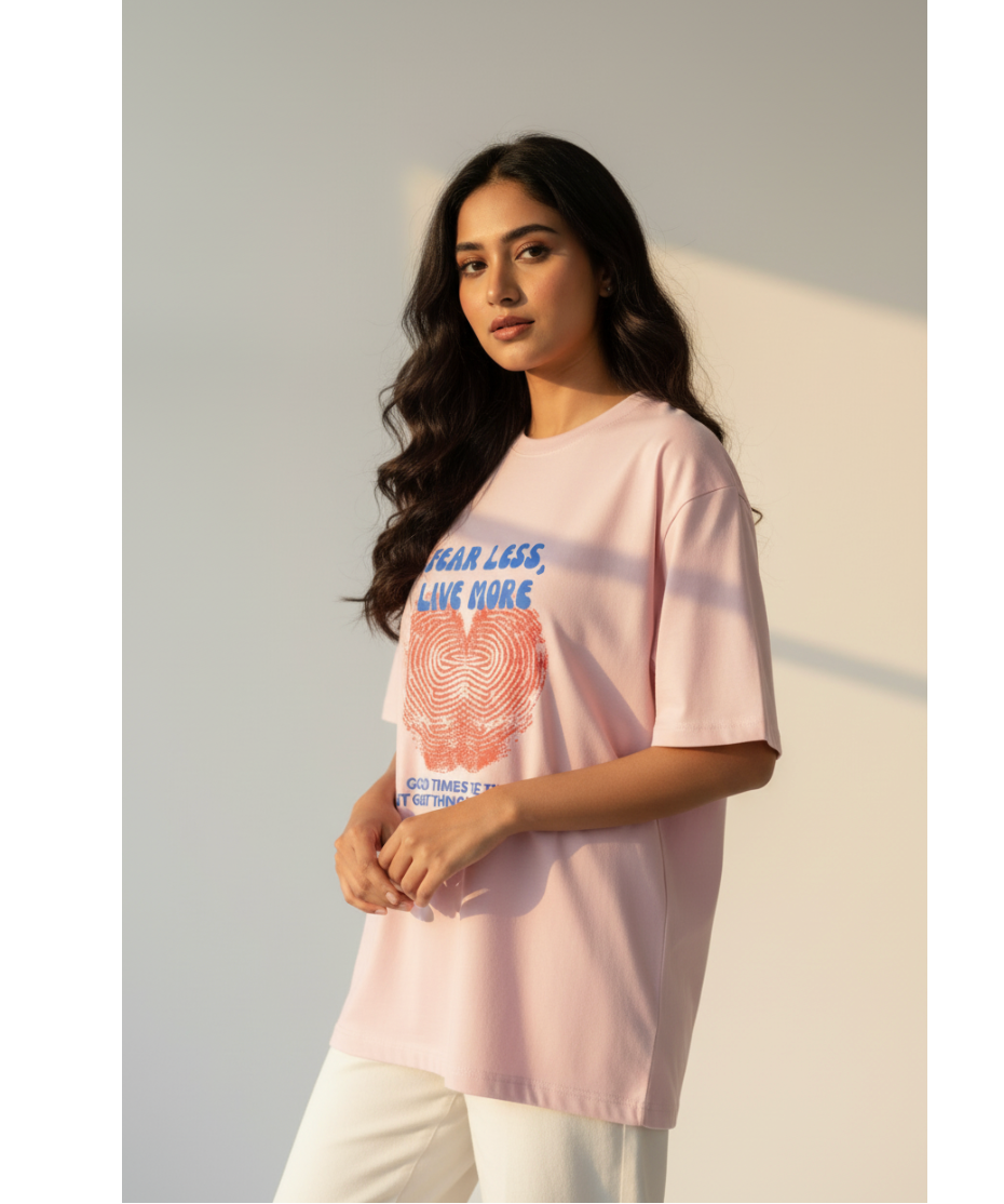 Woman wearing a light pink t-shirt with graphic design and text, standing against a neutral background.